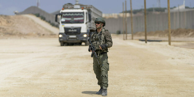 Soldat mit Gewehr steht am Grenzübergang Erez, dahinter ein Lkw.